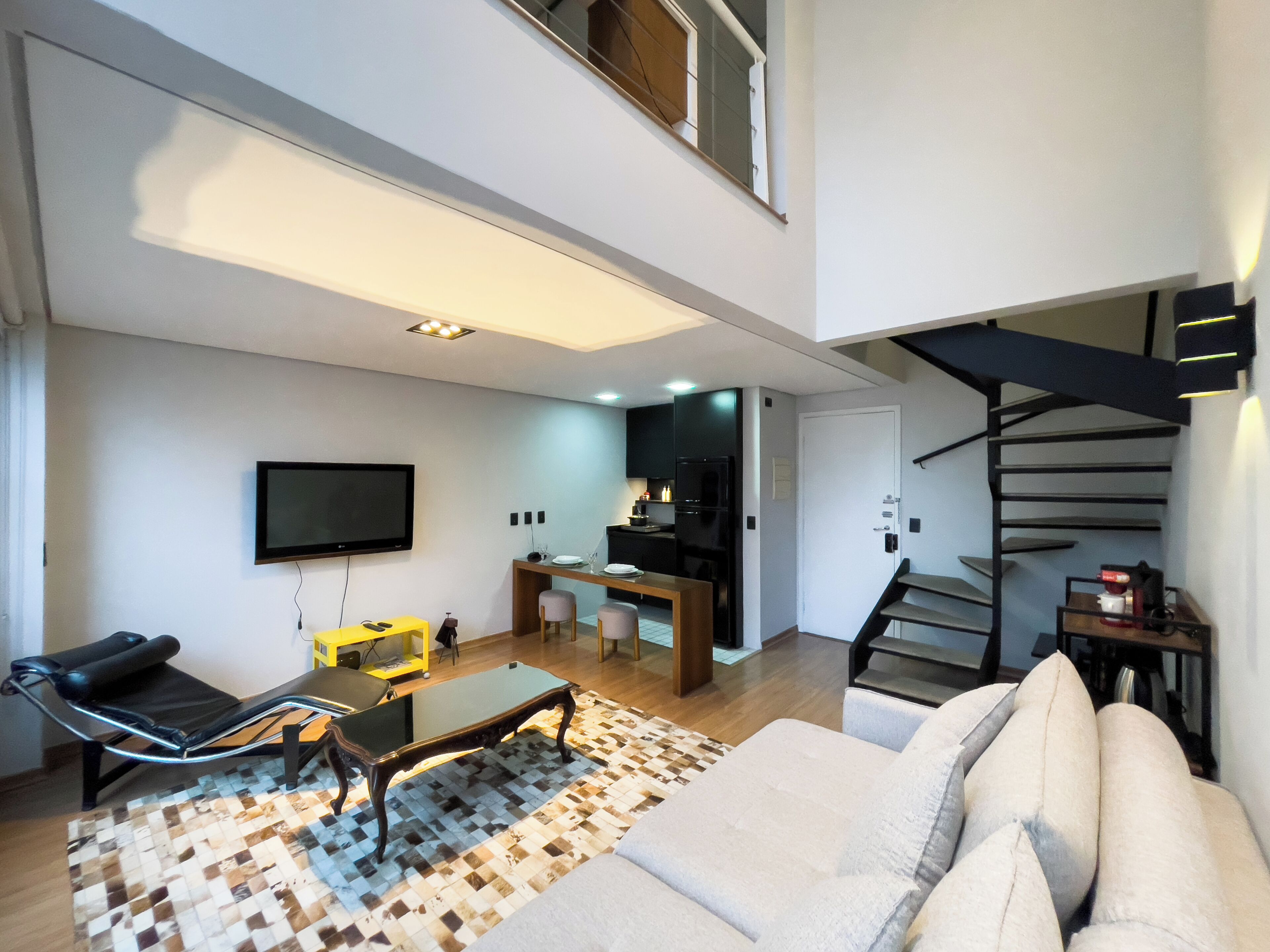 Ein modernes Wohnzimmer mit einer Couch, einem Couchtisch und einem Fernseher. Eine Treppe führt zu einer oberen Ebene.