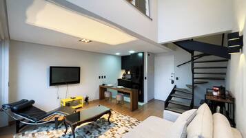 A modern living room with a sofa, a coffee table, and a TV. There's a staircase leading to an upper level.