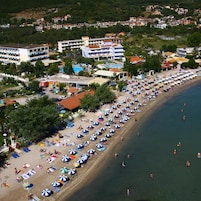Um resort à beira-mar com extensa faixa de areia, vários guarda-sóis e área de piscina.