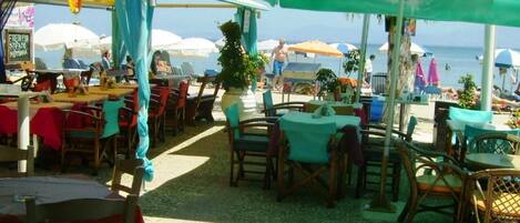 An outdoor seating area with tables and chairs, umbrellas, and a view of the beach.