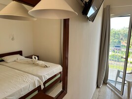 Habitación de hotel con cama, televisor montado en la pared y balcón con vistas a zonas verdes y un coche estacionado.