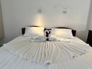 Una cama bien hecha con sábanas blancas y una toalla dispuesta en forma de corazón en el centro.