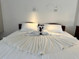 Uma cama bem arrumada com lençóis brancos e uma arrumação de toalhas em formato de coração no centro.