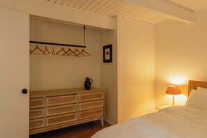 A bedroom with a wooden dresser, a bedside table with a lamp, and a bed with white bedding. - Cozy A-Frame Retreat w/Fireplace & View (Crestline)