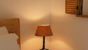 Uma cama com lençóis brancos, uma mesinha com abajur e um espelho com moldura de madeira na parede.