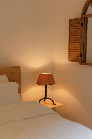 Ein Bett mit weißer Bettwäsche, ein kleiner Tisch mit einer Lampe und ein rahmengenannter Spiegel an der Wand.