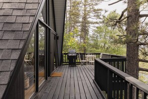 A wooden deck with a grill, outdoor seating, and a view of trees. - Cozy A-Frame Retreat w/Fireplace & View (Crestline)