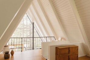 Una habitación con techo inclinado, un escritorio de madera y un ventanal con vistas a árboles.