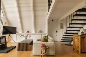 A living room with a high ceiling, a fireplace, a television, and a staircase. - Cozy A-Frame Retreat w/Fireplace & View (Crestline)
