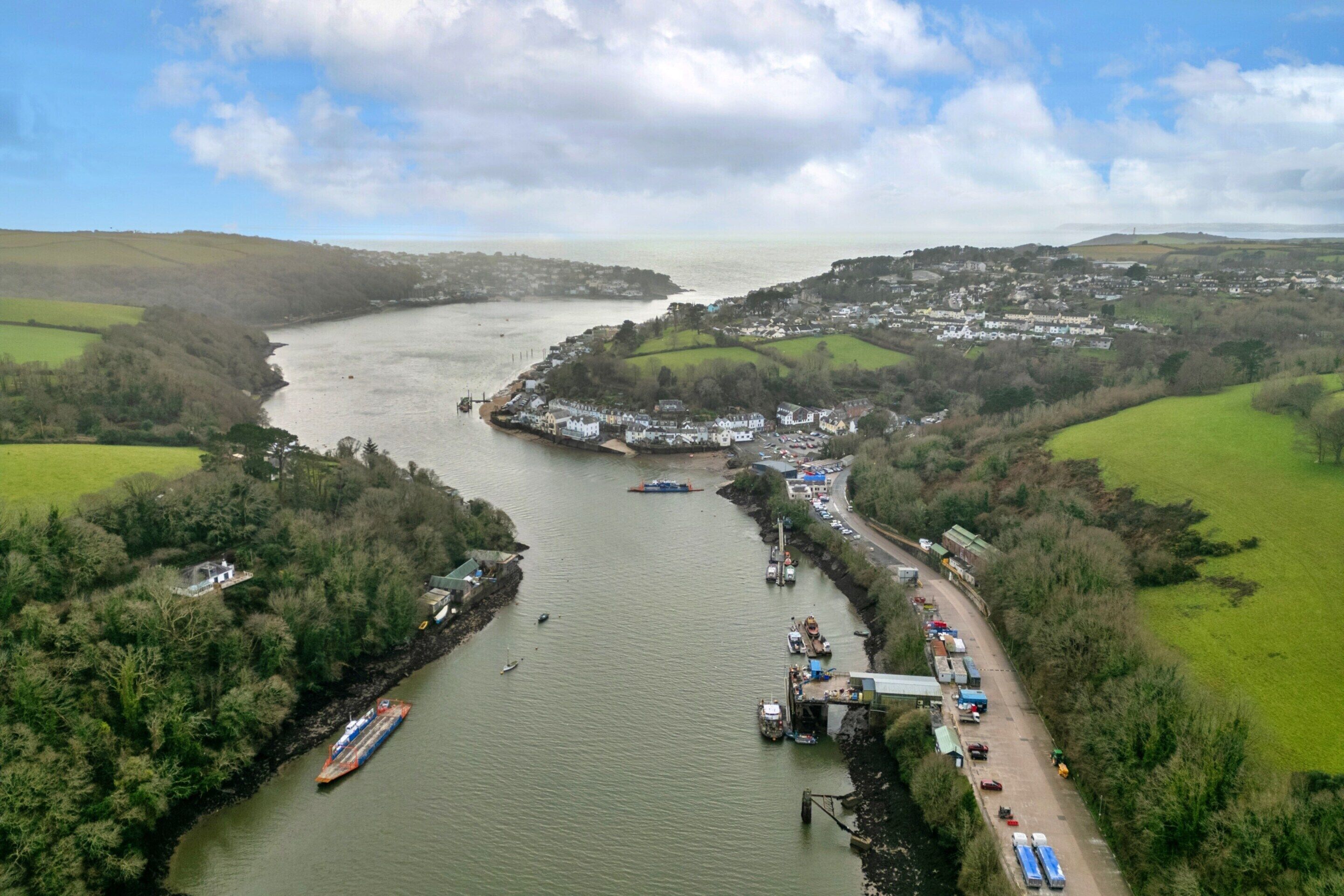 A river with a dock and boats, surrounded by green fields and a small town.