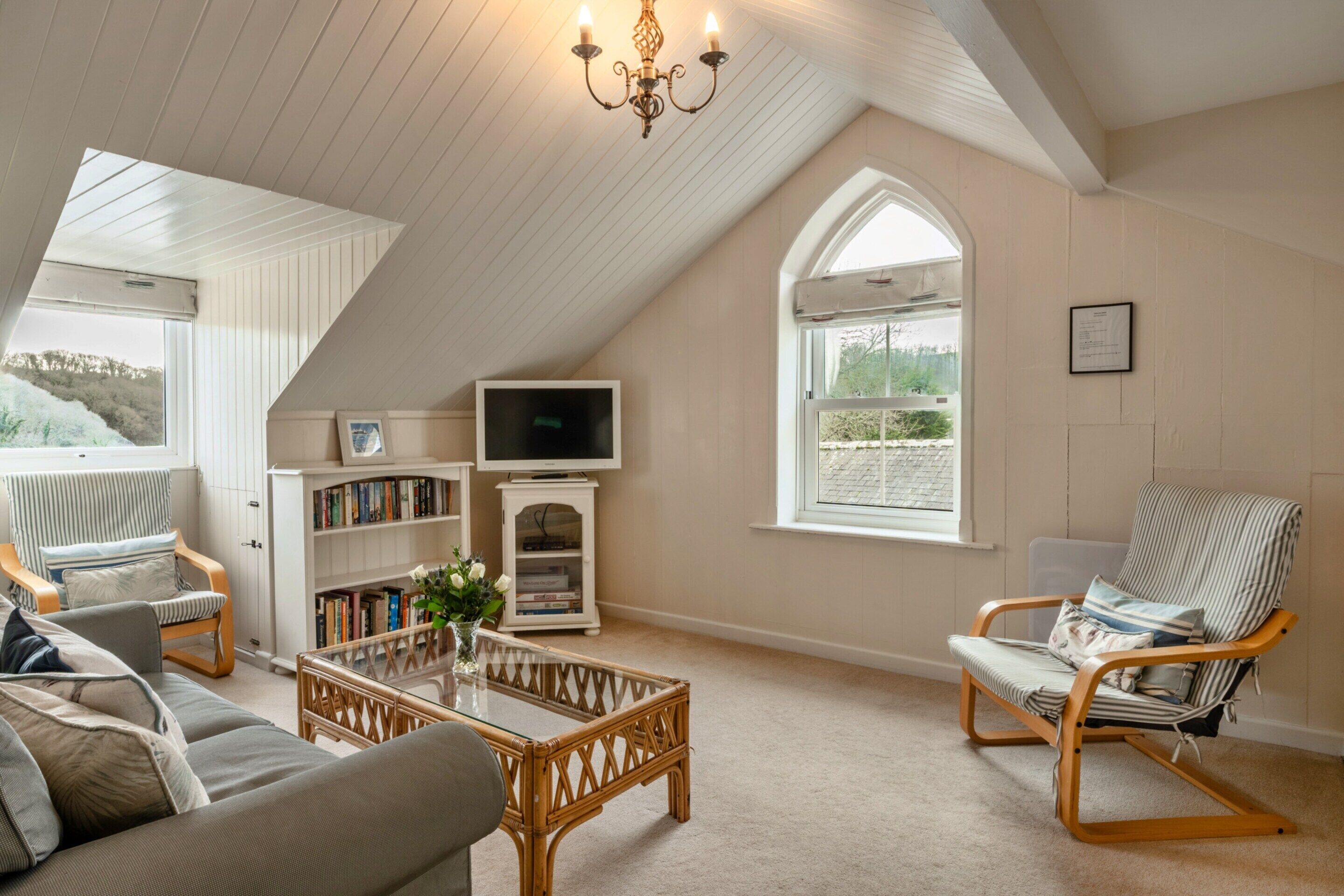 A cozy loft-style living room with a sloped ceiling, a television, a bookshelf, and two lounge chairs.