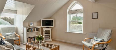 A cozy loft-style living room with a sloped ceiling, a television, a bookshelf, and two lounge chairs.