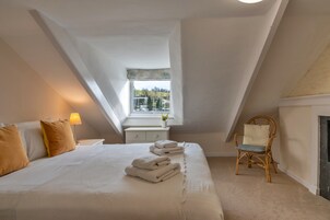 Une chambre à coucher avec un lit, une table de chevet, une lampe, une fenêtre, une chaise et une cheminée.