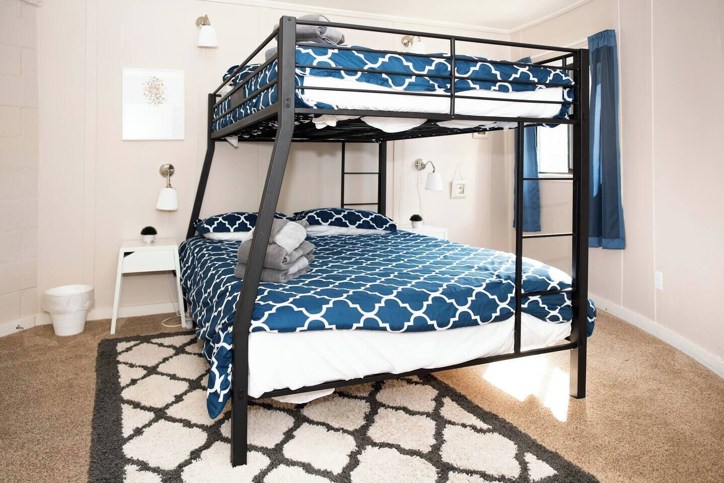 Una cama litera con una colcha estampada, una mesita de noche pequeña con una lámpara y un cuadro colgado en la pared.