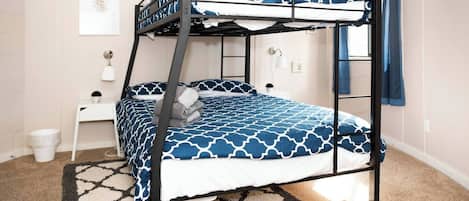 Una cama litera con una colcha estampada, una mesita de noche pequeña con una lámpara y un cuadro colgado en la pared.