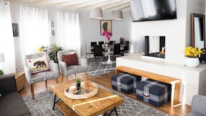 Ein modernes Wohnzimmer mit Sofa, Couchtisch, Hocker, Kamin und an der Wand befestigtem Fernseher.