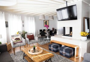 Ein modernes Wohnzimmer mit Sofa, Couchtisch, Hocker, Kamin und an der Wand befestigtem Fernseher.