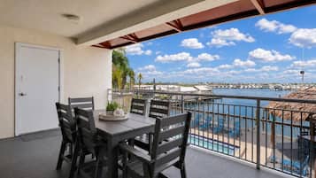 Varanda com mesa e cadeiras, vista para uma marina com barcos e céu claro.