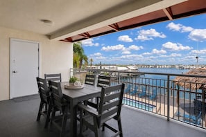 Varanda com mesa e cadeiras, vista para uma marina com barcos e céu claro.