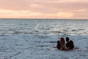 Ein Paar sitzt bei Sonnenuntergang auf einer Badematte und blickt aufs Meer.