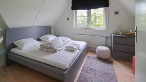 A bedroom with a bed, a window with a view, a radiator, a bedside table, and a dresser. - Waterfront Beach Villa for 5 (Makkum)