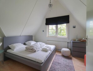 A bedroom with a bed, a window with a view, a radiator, a bedside table, and a dresser. - Waterfront Beach Villa for 5 (Makkum)