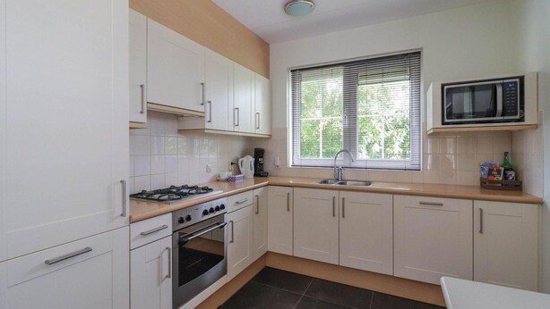 A kitchen with white cabinets, a gas stove, an oven, a microwave, and a window with blinds. - Waterfront Beach Villa for 5 (Makkum)