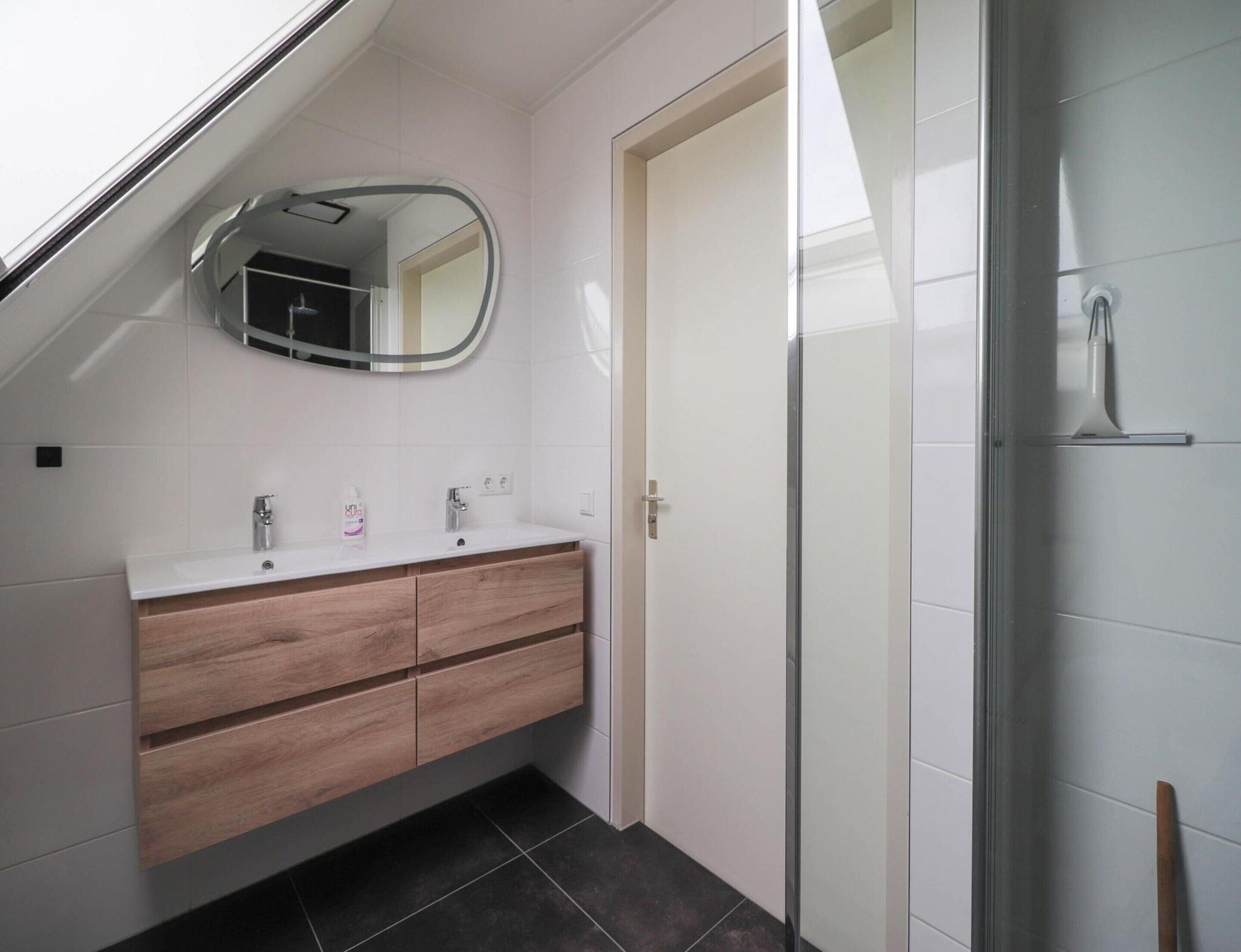 Een moderne badkamer met dakraam, een dubbele wastafel met spiegel en een douchecabine van glas.