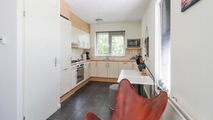 A compact kitchen with white cabinets, a microwave, and a window with blinds. - Waterfront Beach Villa for 5 (Makkum)