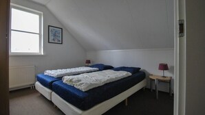 A bedroom with a sloped ceiling, a bed with blue bedding, a small bedside table with a lamp, and a window with a picture on the wall. - Beachside Dune Villa With Garden (Makkum)