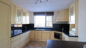 A kitchen with light-colored cabinets, a black countertop, and a window with blinds. - Beachside Dune Villa With Garden (Makkum)