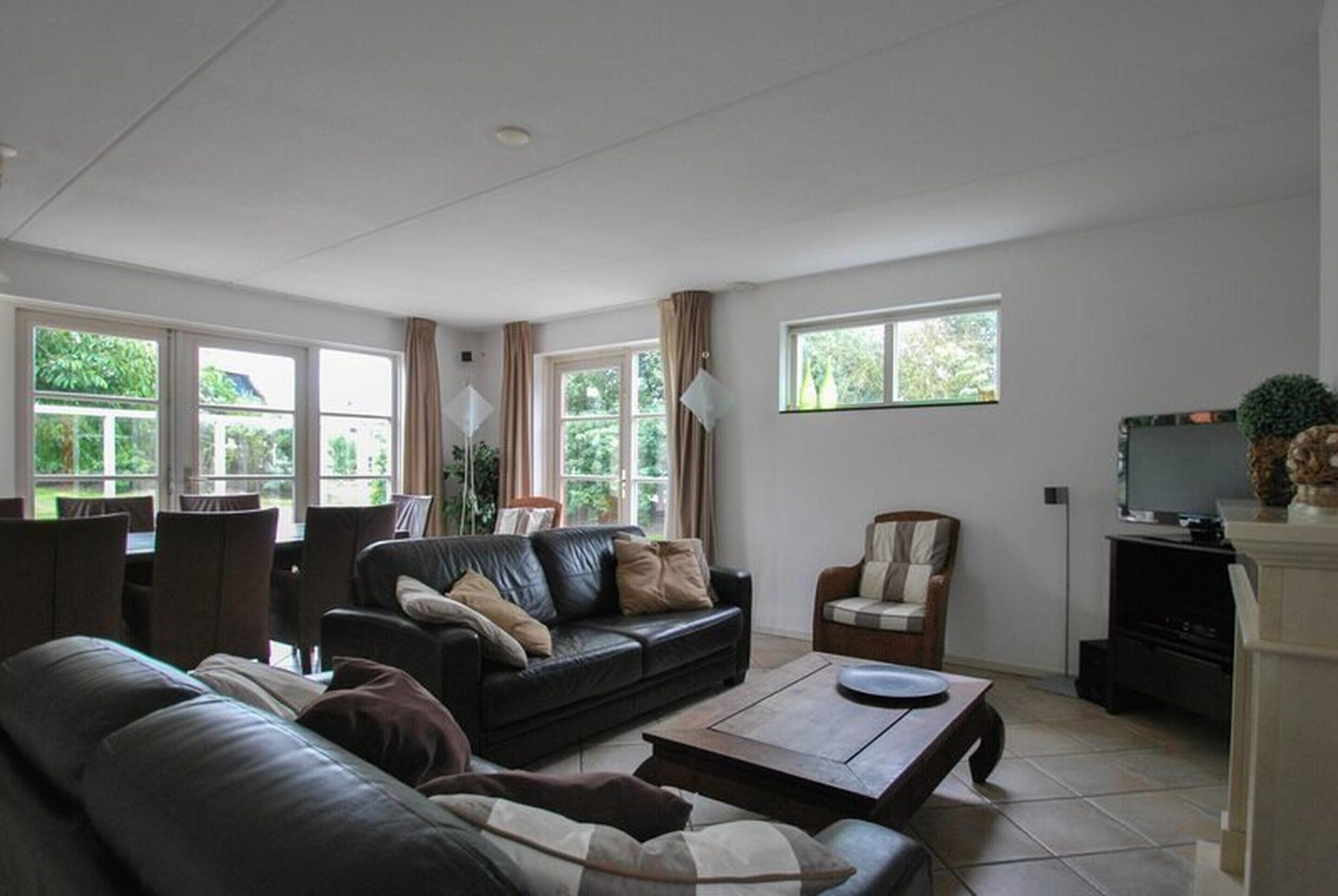 A living room with a black leather sofa, a wooden coffee table, a dining table with chairs, and a television on a stand.