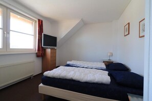 Une chambre à coucher avec un lit, une télévision, une fenêtre avec des rideaux et un radiateur.