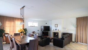 A modern living room with a dining area, a fireplace, a flat-screen TV, and a sofa. - Beachside Dune Villa With Garden (Makkum)