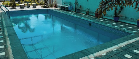 Piscina rectangular con borde alicatado, rodeada de plantas en macetas y mobiliario de exterior.