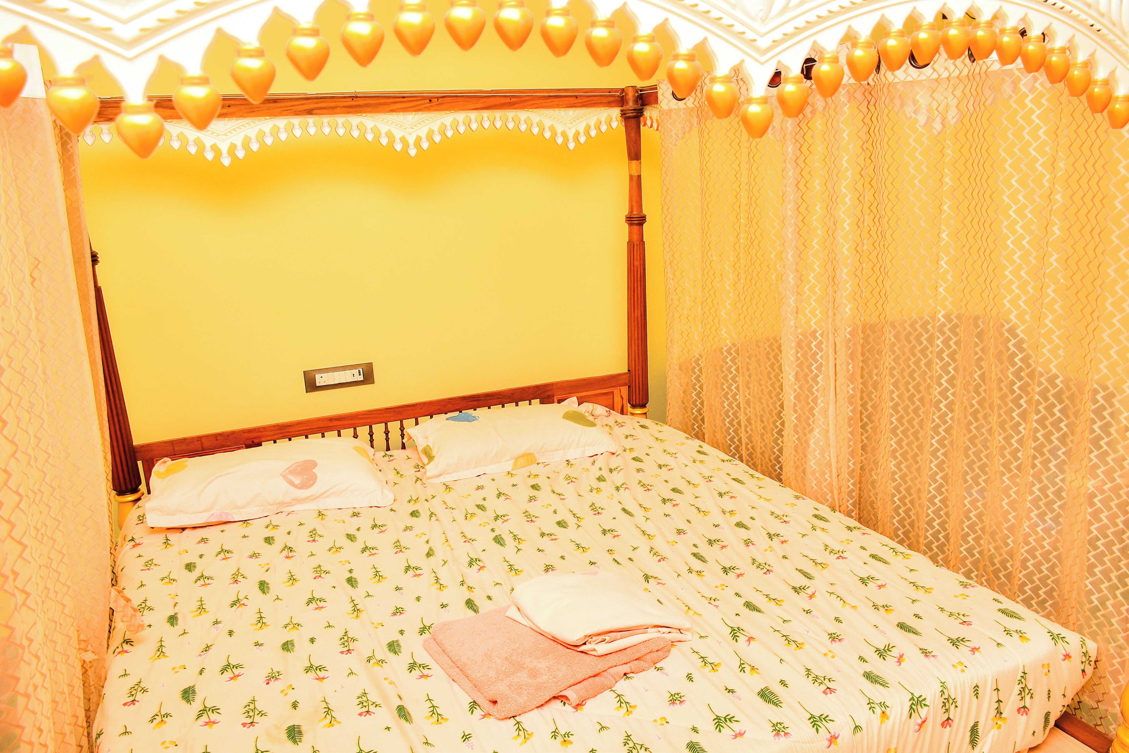 A bed with a floral-patterned bedspread, a wooden headboard, and a wall-mounted light switch.