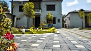 Un edificio residencial con entrada central, un pequeño jardín con fuente y un camino de entrada pavimentado.