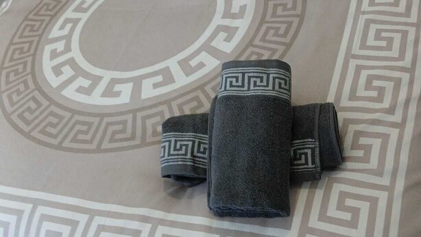 Een bed met een beddekleed met patroon en twee kussens, een opgevouwen handdoek en een bijpassende hoofdband.
