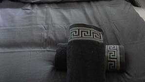 Una cama con edredón gris, una almohada a juego y una toalla enrollada con diseño geométrico.