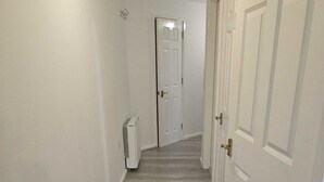 Un pasillo con piso de madera, paredes blancas y una puerta blanca al final.