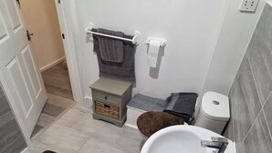 Un baño con lavamanos blanco, inodoro y una mesita de noche pequeña con una cesta.
