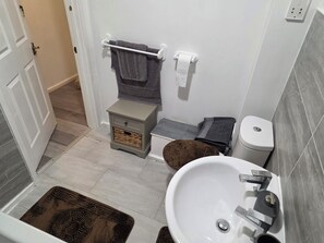 Un bany amb un lavabo blanc, un vàter i una petita taula de nit amb un cisteller.