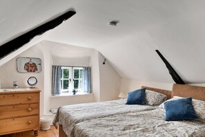 A bedroom with a sloped ceiling, a wooden dresser, a bed with floral bedding, and a window with curtains. - River Avon Stay for Four (Totnes)