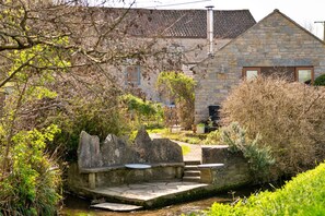 Ein Steinhaus mit einem Ziegeldach, ein kleiner Garten mit einer Steinsitzbank und ein schmaler Kanal.