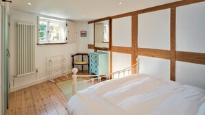 A bedroom with a wooden floor, a white radiator, a window, a chair, a dresser, and a bed. - Elegant Apartment in Regency Cheltenham (Somerton)