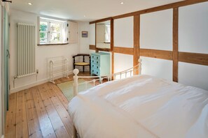 Ein Schlafzimmer mit Holzboden, einem weißen Heizkörper, einem Fenster, einem Sessel, einem Schminktisch und einem Bett.