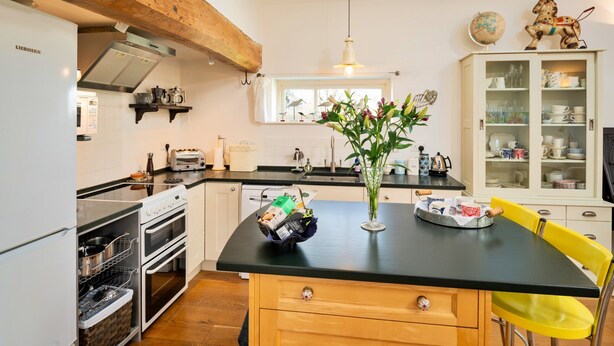 A kitchen with wooden cabinets, a black countertop, a stove, and a window with a view. - Elegant Apartment in Regency Cheltenham (Somerton)