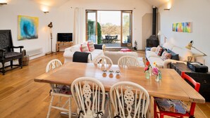 A spacious living area with a wooden dining table, white chairs, a sofa, and a television. - Elegant Apartment in Regency Cheltenham (Somerton)