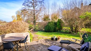 A stone patio with a round table and chairs, surrounded by a garden with various plants and a lawn. - Elegant Apartment in Regency Cheltenham (Somerton)