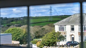 A rural landscape with a house, a car, and a wind turbine in the distance. - Modern Studio Near Port Isaac (Bodmin)